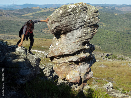 Woman walking in a rocky mountain, leaning against a face-shaped rock, vegetation at its base, located in the Três Barras region, municipality of Serro, Minas Gerais. photo