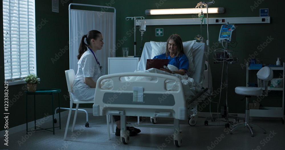 Fototapeta premium Doctor seated beside elderly patient, providing document for her to sign.