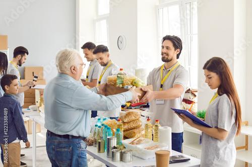 Happy volunteer at the aid center gives an old man a box of food, close-up. Group of volunteers working on a humanitarian project. Concept canned food, humanitarian aid, non-profit organization
