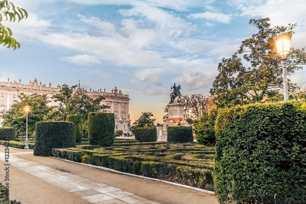 Fototapeta premium The lush gardens of Plaza de Oriente in Madrid, Spain, with the equestrian statue of King Philip IV in the distance. The beautifully trimmed hedges and evening light create a serene atmosphere