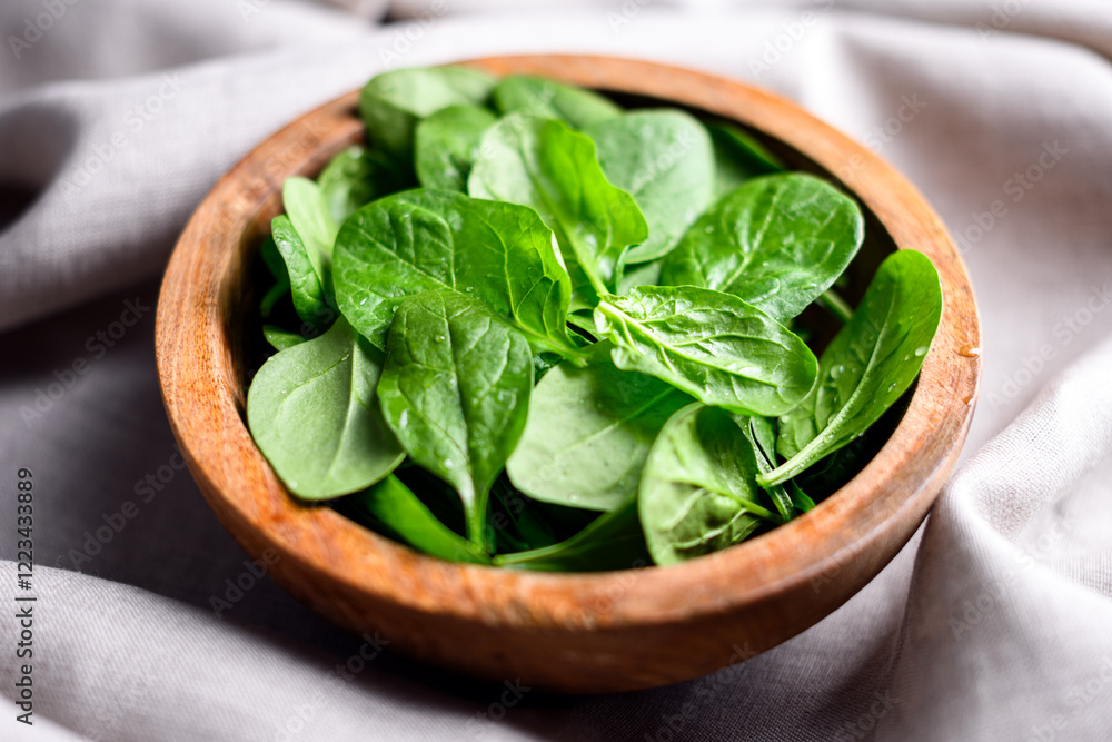 Heap of baby spinach leaves with water drops in a wooden bowl on linen tablecloth. Raw organic spinach greens close up Heap of baby spinach leaves with water drops in a wooden bowl on linen tablecloth. Raw organic spinach greens close up