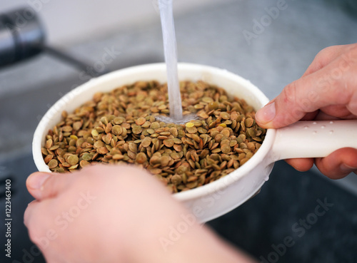 Fotografija A woman rinsing green lentils in a sieve. Close up.