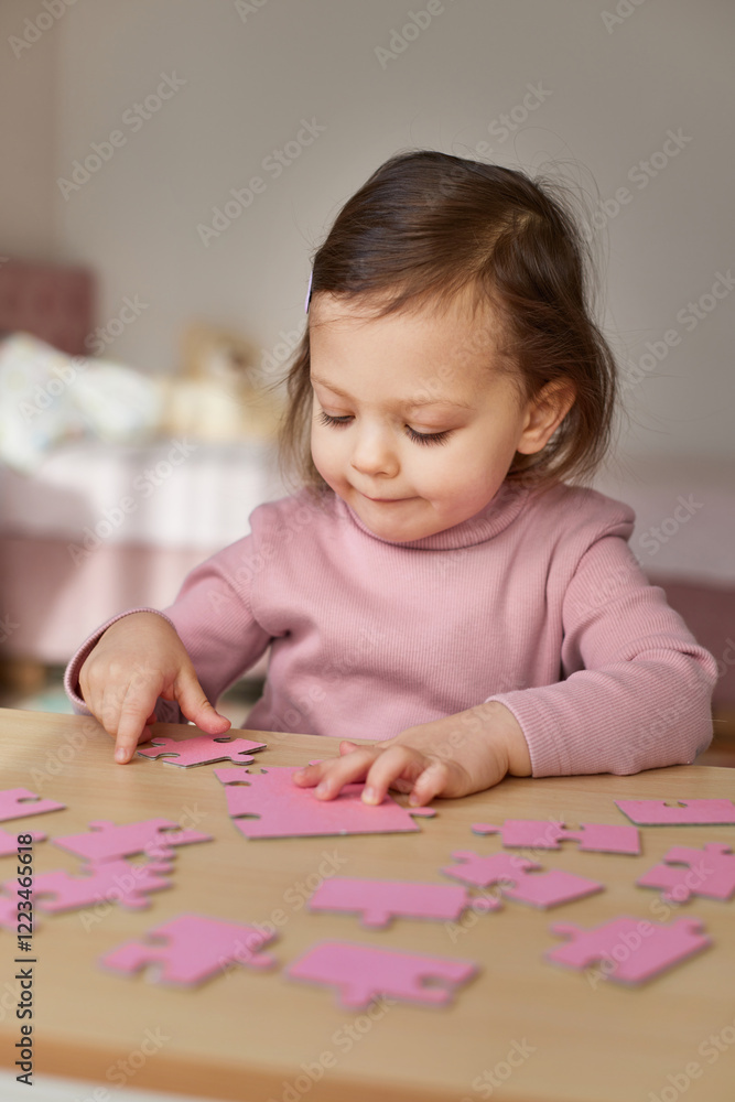 Cute baby girl connecting puzzle pieces on wooden desk in room Cute baby girl connecting puzzle pieces on wooden desk in room