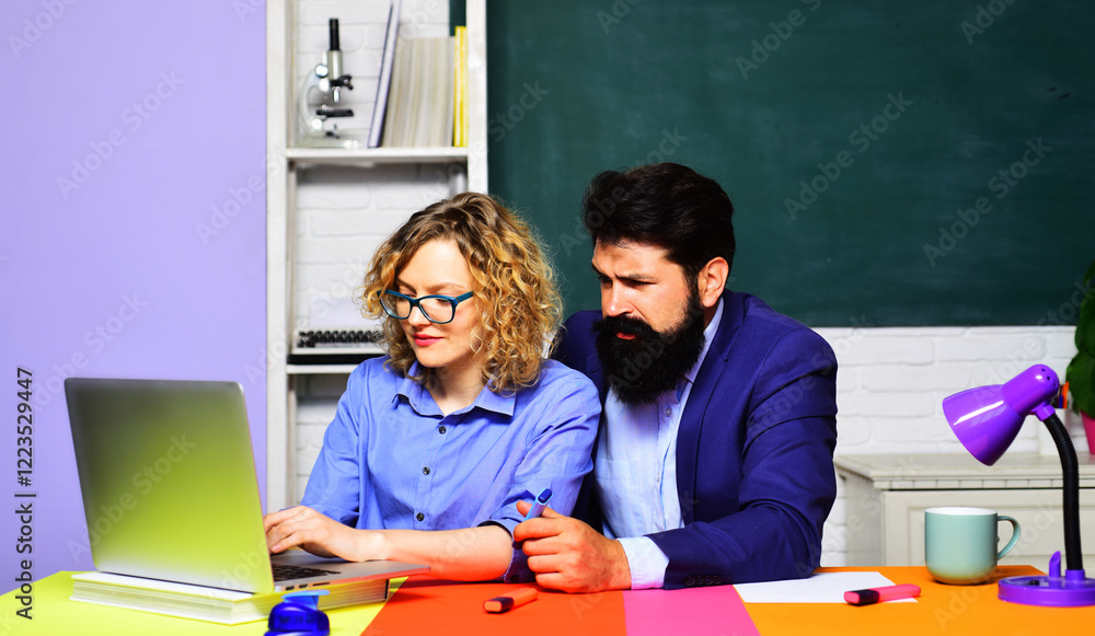 Couple of teachers on exam or test in classroom. Students doing homework, searching information on network, making project online. Female student and male teacher working with laptop in university. Couple of teachers on exam or test in classroom. Students doing homework, searching information on network, making project online. Female student and male teacher working with laptop in university.