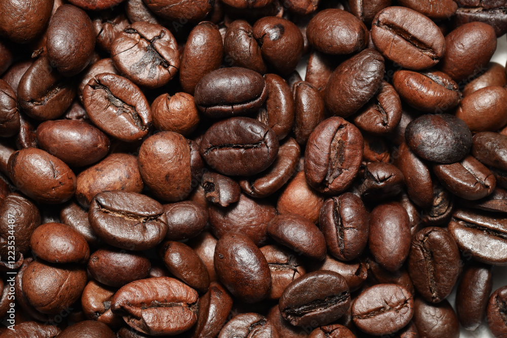 Fototapeta premium A macro close-up of roasted coffee beans showcasing their rich brown color, detailed texture, and natural oils. The beans are tightly packed, emphasizing their unique shapes and surface patterns.