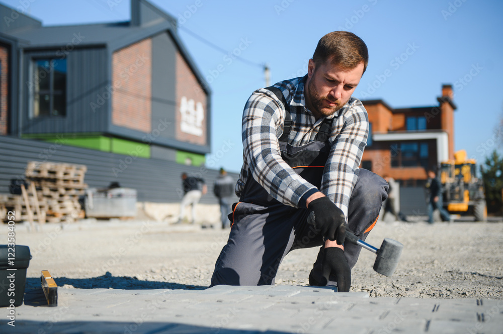 Builder laying a paving brick placing it on the sand foundation with gloved hands Builder laying a paving brick placing it on the sand foundation with gloved hands