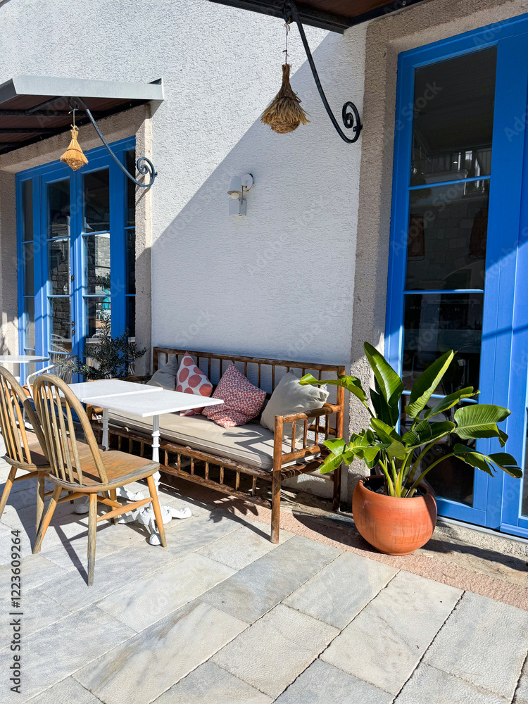 Obraz premium Cozy outdoor seating area with plants and bright blue doors in a sunlit courtyard