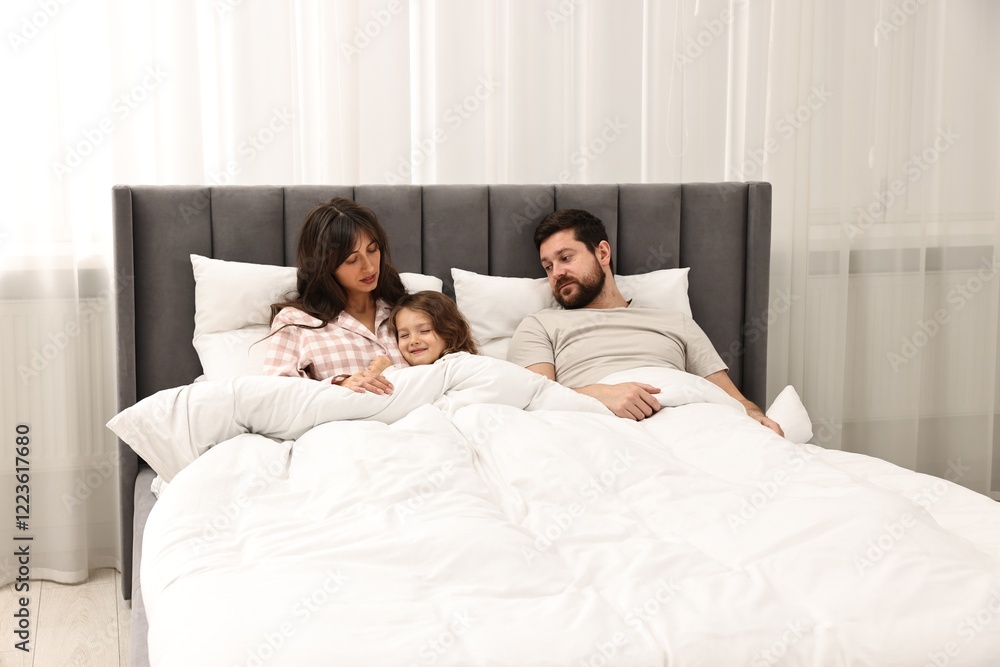 Fototapeta premium Playful daughter with her overwhelmed parents in bed at home