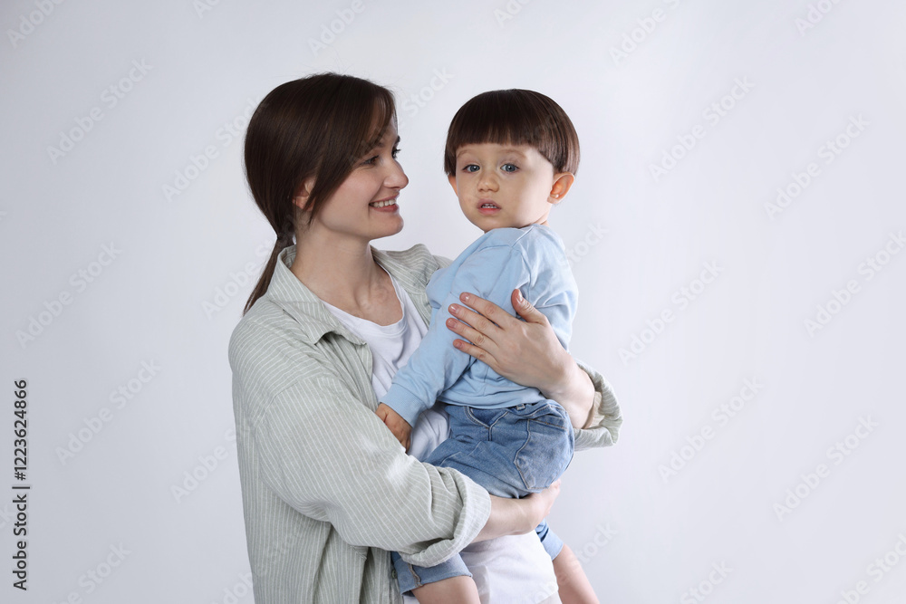 Beautiful mother with her cute little son on light grey background Beautiful mother with her cute little son on light grey background