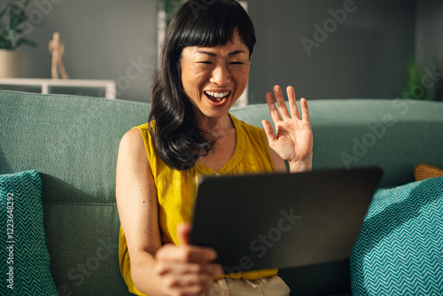 Asian woman joyfully using her tablet for a video call conversation. photo