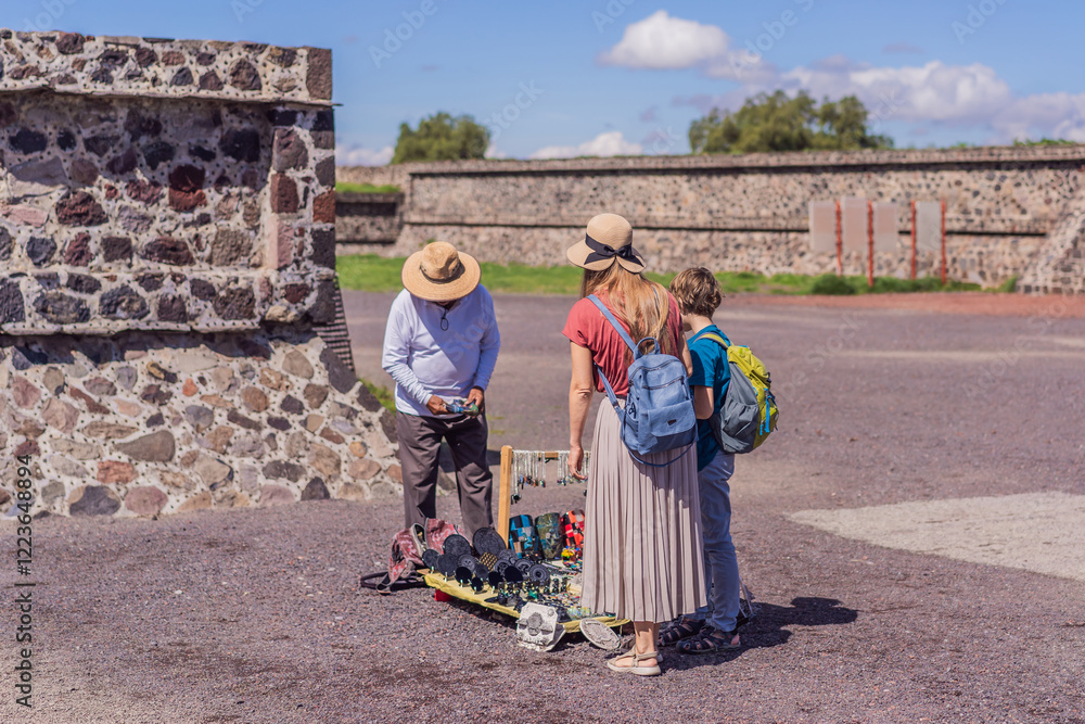 Mother and son tourists buying Mexican souvenirs from a street vendor at the foot of the Teotihuacan pyramid. Cultural experience, travel, and local craftsmanship concept