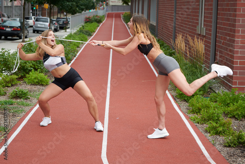 Εκτύπωση καμβά Two beautiful young women pose outside in workout attire on track playfully pull