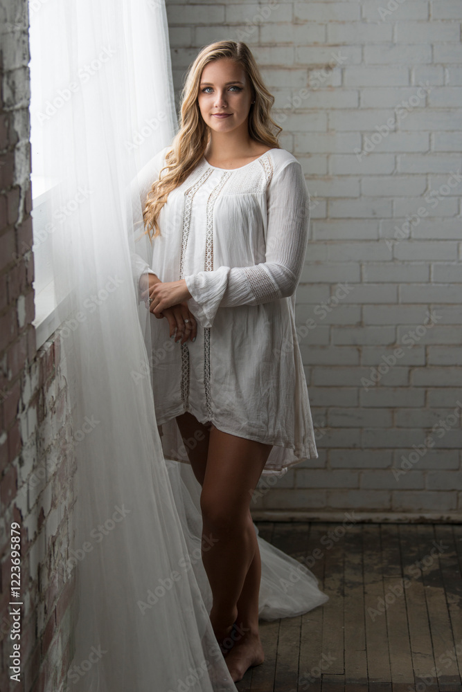 Fototapeta premium Sexy young blonde woman stands near window wearing lace dress