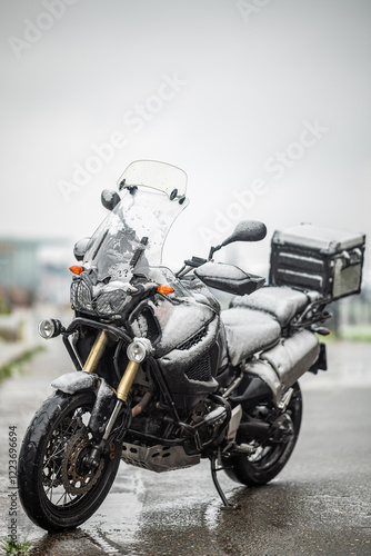 A large black touring motorcycle is covered in snow. The end of the motorcycle season, winter. The inscriptions 