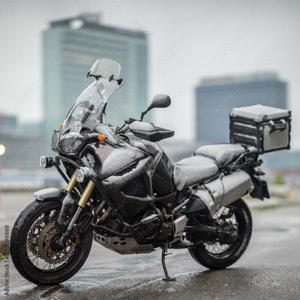 A large black touring motorcycle is covered in snow. The end of the motorcycle season, winter. The inscriptions 