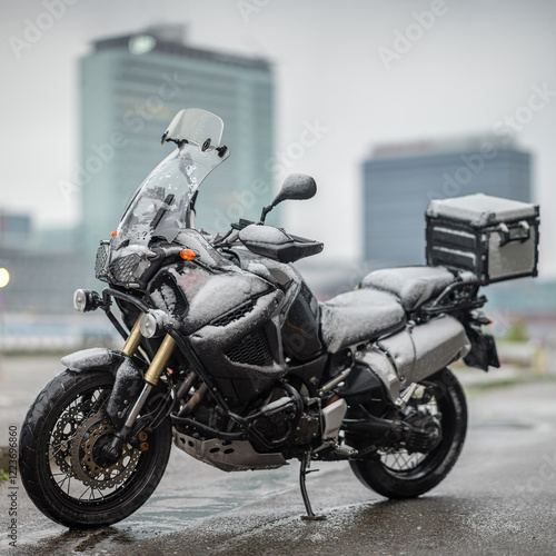 A large black touring motorcycle is covered in snow. The end of the motorcycle season, winter. The inscriptions 
