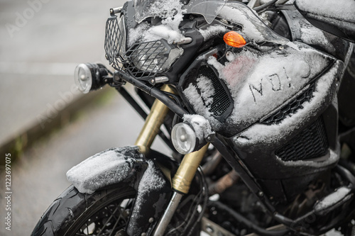 A large black touring motorcycle is covered in snow. The end of the motorcycle season, winter. The inscriptions 