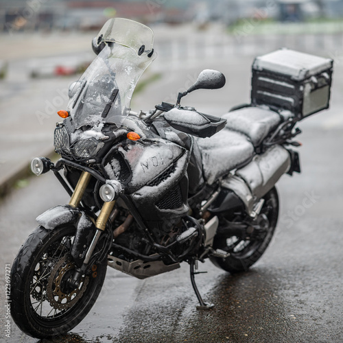 A large black touring motorcycle is covered in snow. The end of the motorcycle season, winter. The inscriptions 