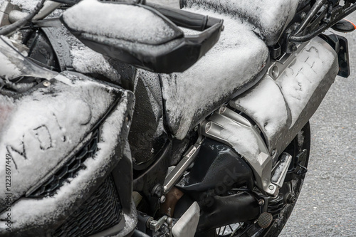 A large black touring motorcycle is covered in snow. The end of the motorcycle season, winter. The inscriptions 