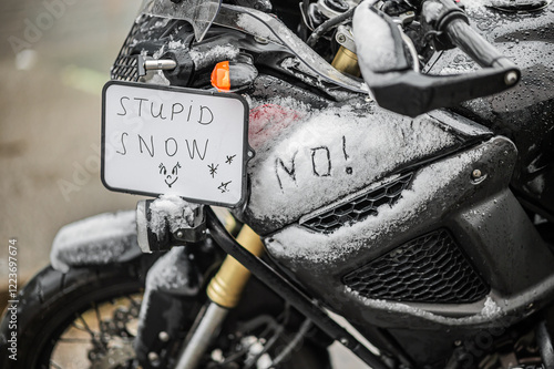 A large black touring motorcycle is covered in snow. The end of the motorcycle season, winter. The inscriptions 