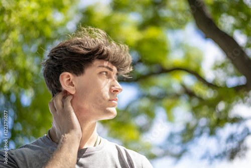 Confident young blonde man portrait, summer trees background.