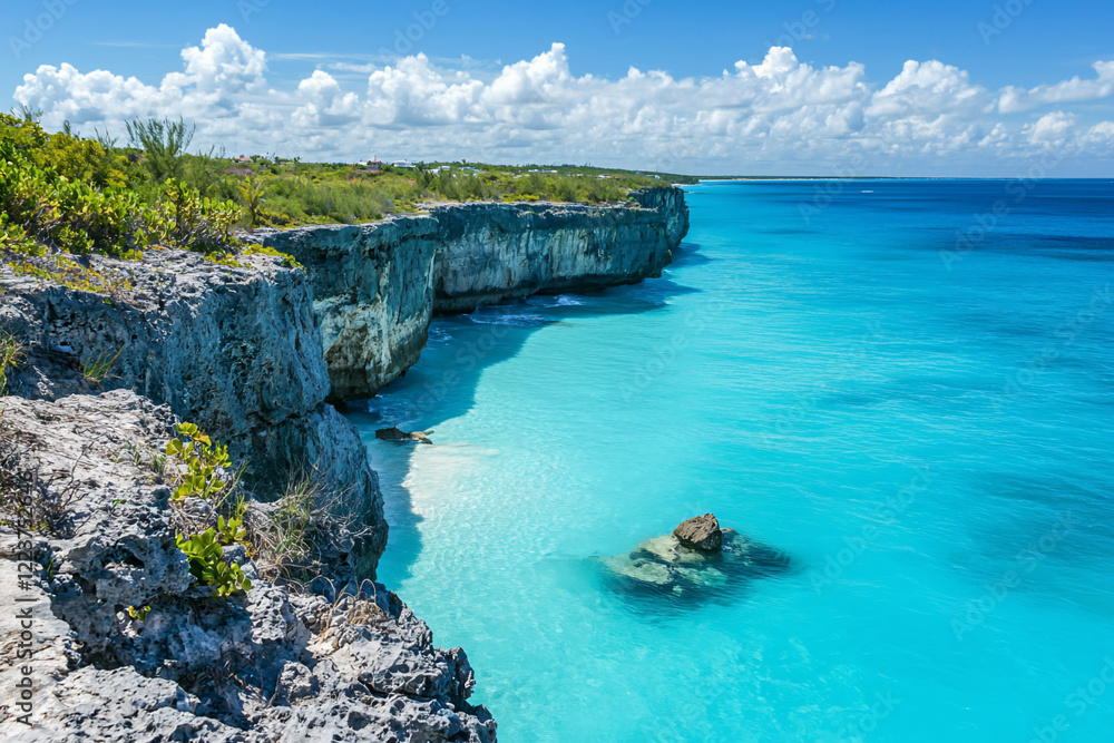 Fototapeta premium Serene coastal landscape featuring turquoise waters, rocky cliffs, and a clear blue sky under clouds