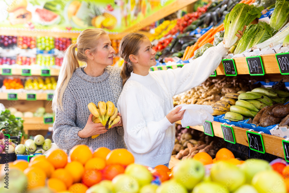 Obraz premium Positive woman and teenage girl shopping vegetables and fruits at the grocery shop