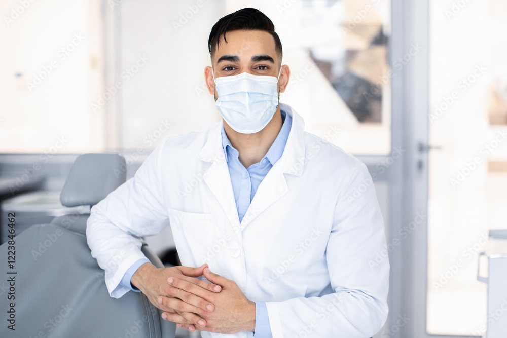 Portrait Of Young Middle Eastern Dentist Wearing Protective Medical Mask Posing At Workplace In Modern Dental Clinic, Arab Stomatologist In Uniform Looking At Camera, Ready For Check Up With Patient Portrait Of Young Middle Eastern Dentist Wearing Protective Medical Mask Posing At Workplace In Modern Dental Clinic, Arab Stomatologist In Uniform Looking At Camera, Ready For Check Up With Patient