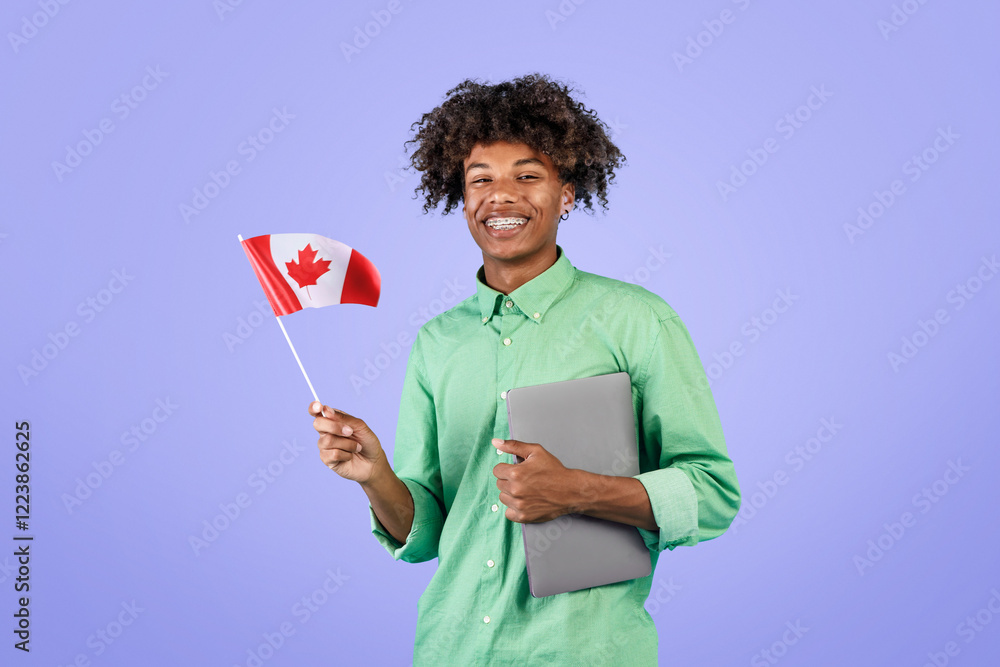 Modern education and student exchange. Happy black guy with laptop holding small flag of Canada and smiling at camera, standing over blue background, studio shot, copy space Modern education and student exchange. Happy black guy with laptop holding small flag of Canada and smiling at camera, standing over blue background, studio shot, copy space