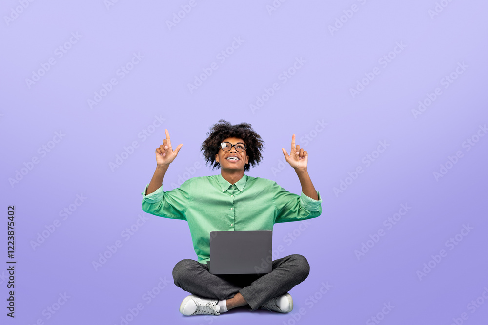 Check this. Black teen guy sitting with laptop and pointing up at free space above head over blue background, crop. Cheerful male student showing empty place for your text Check this. Black teen guy sitting with laptop and pointing up at free space above head over blue background, crop. Cheerful male student showing empty place for your text