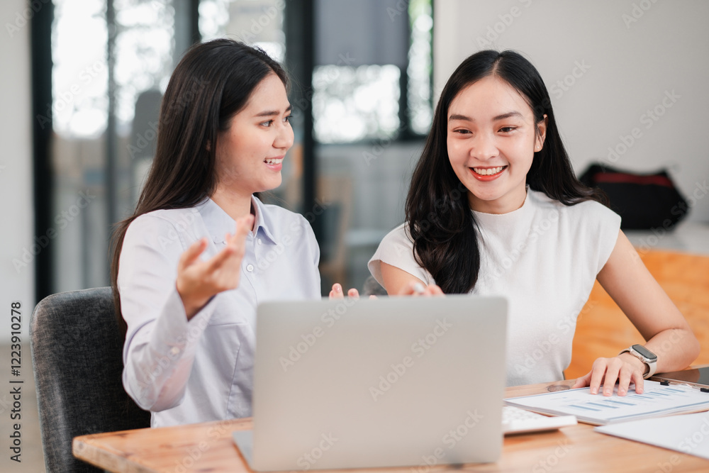 Two women engaged in a business discussion at a contemporary office, using a laptop and reviewing documents. Two women engaged in a business discussion at a contemporary office, using a laptop and reviewing documents.
