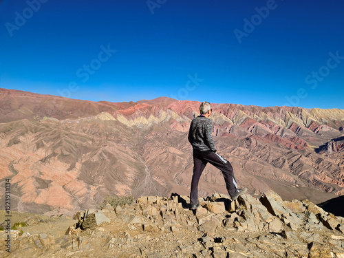 Elderly man looking at mountain with folded colorful rocks photo