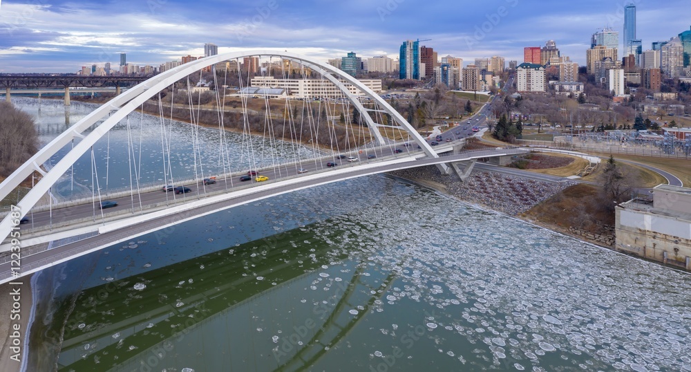 Naklejka premium Aerial view of the Walterdale Bridge over the river, cars on the road, and ice patterns on the water. Cityscape in the background. Edmonton, Alberta, Canada