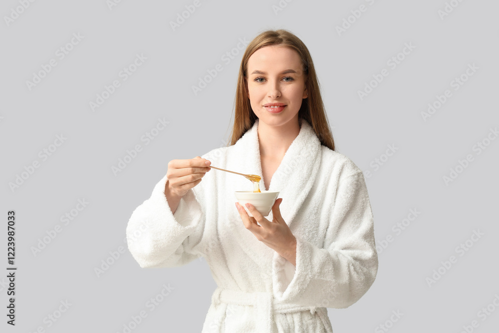 Beautiful young happy woman holding bowl and spatula with sugaring paste on grey background Beautiful young happy woman holding bowl and spatula with sugaring paste on grey background