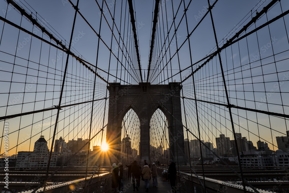 Fototapeta premium brooklyn bridge at sunrise (new york city landmark over east river to manhattan) travel tourism famous destination in usa america united states (suspension cables lamp light streetlight) people cross