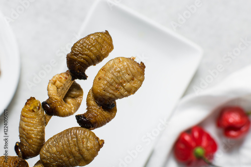 Overhead view of roasted sago worms, top view of palm worms on white background, roasted grub worms photo