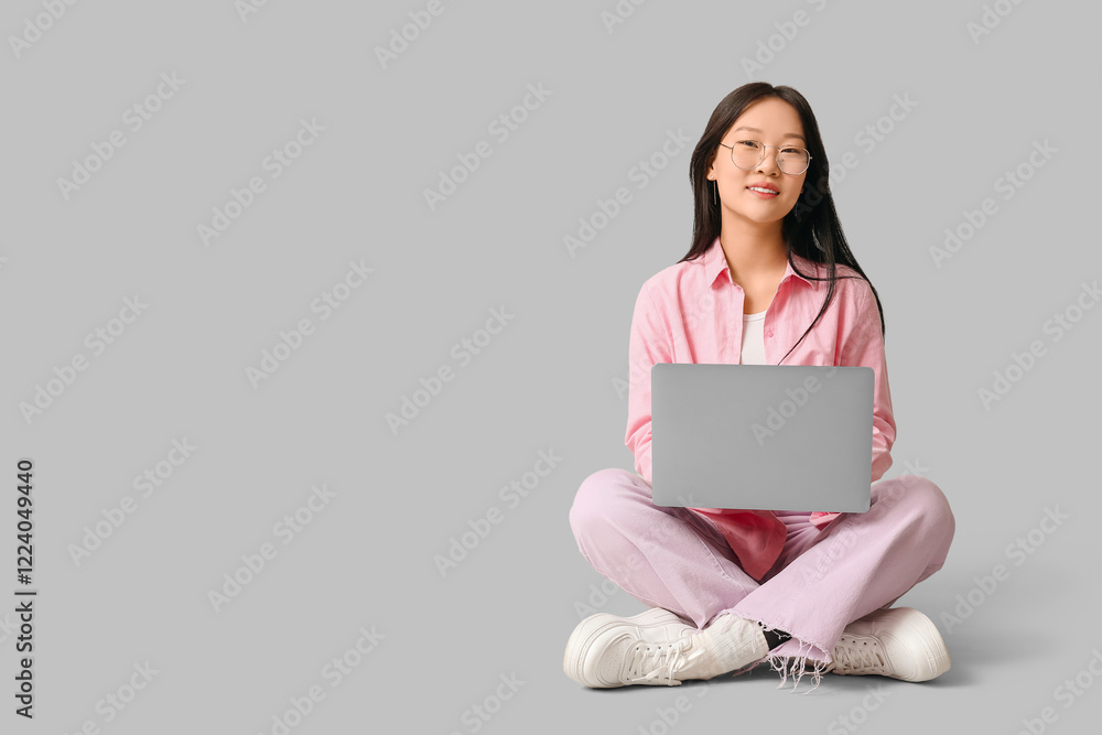 Naklejka premium Beautiful young Asian woman with modern laptop sitting on grey background