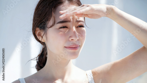 眩しい夏の日差しからを遮るよう、手をかざし目を細めている日本人女性、白背景