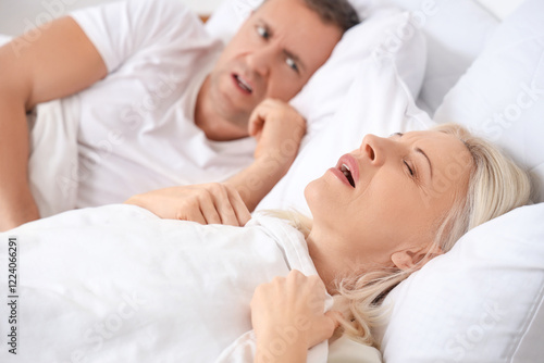 Snoring mature woman with her irritated husband in bedroom, closeup photo