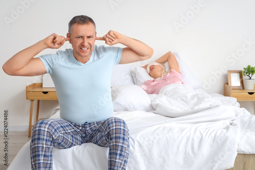 Irritated mature man covering his ears because of wife's snoring in bedroom photo