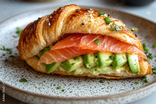 A croissant sandwich filled with avocado slices and smoked salmon on a round plate. (Generative AI)