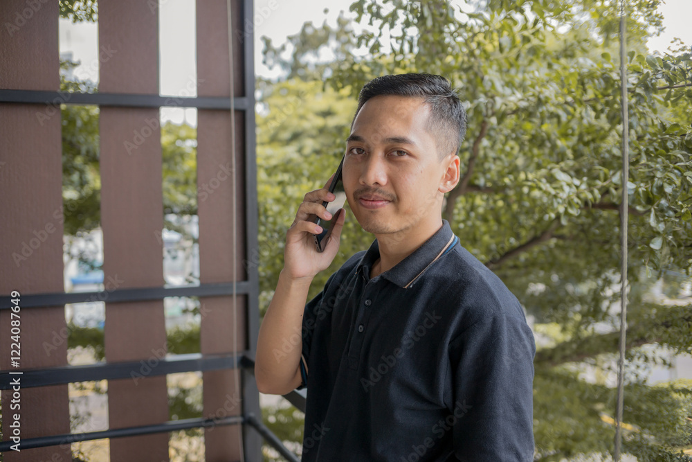 Man Standing And Making A Phone Call With A Smile, Looking To The Side In A Quiet, Calm Environment, Fully Engaged In Conversation. Man Standing And Making A Phone Call With A Smile, Looking To The Side In A Quiet, Calm Environment, Fully Engaged In Conversation.