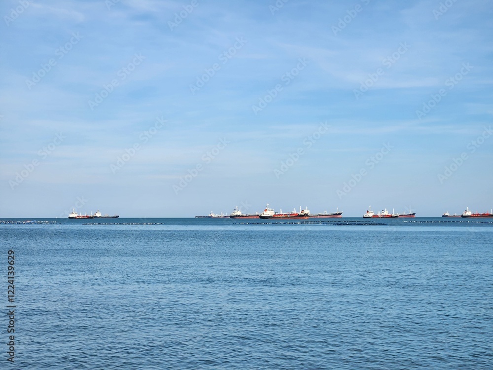 Fleet of Cargo Ships: A fleet of cargo ships traverses the open sea, their silhouettes cutting through the blue expanse against a backdrop of a serene sky. Fleet of Cargo Ships: A fleet of cargo ships traverses the open sea, their silhouettes cutting through the blue expanse against a backdrop of a serene sky.