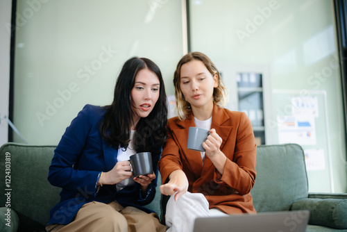 Two women collaborating on a project on sofa at home, brainstorming with a laptop and notebook