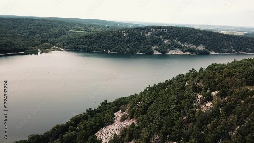 A serene aerial view of Devils Lake surrounded by lush forests and rocky cliffs in Wisconsin's natural landscape. A serene aerial view of Devils Lake surrounded by lush forests and rocky cliffs in Wisconsin's natural landscape.