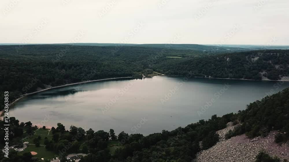 A breathtaking aerial view of Devils Lake in Wisconsin, showcasing its tranquil waters, lush green forests, and surrounding cliffs. A breathtaking aerial view of Devils Lake in Wisconsin, showcasing its tranquil waters, lush green forests, and surrounding cliffs.