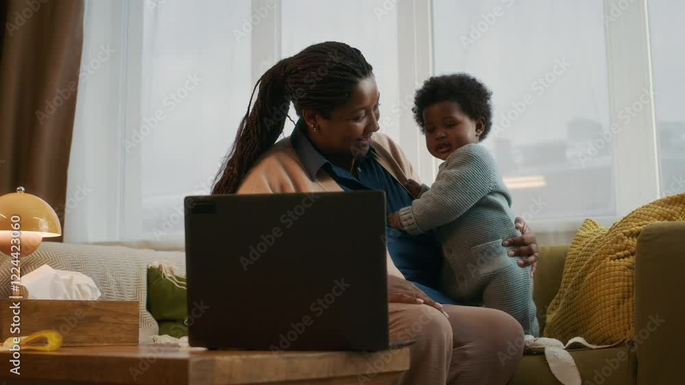 African American toddler smiling and laughing as she watching cartoons on laptop with her mother, while sitting on couch in cozy apartment African American toddler smiling and laughing as she watching cartoons on laptop with her mother, while sitting on couch in cozy apartment