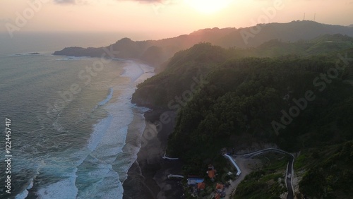 Aerial drone view ofsunset at  the coastline and seashore with rocks, hills and trees, beach sand and waves from the ocean at Surumanis Beach, Kebumen, Central Java, Indonesia photo