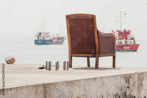 Lonely vintage armchair overlooks a calm sea with distant fishing boats. A serene, slightly melancholic coastal scene evoking themes of solitude and contemplation photo