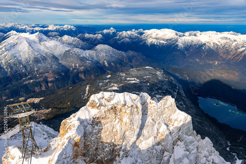 Wide angle panoramic view from Germanys highest peak, the “Zugspitze“ (2962 m) near Garmisch-Partenkirchen (Bavaria) with cable car, the Alpine foothills and Lake Eibsee in the valley with fresh snow. photo